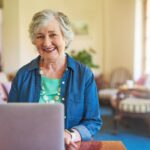 A old woman smiling in front of a laptop