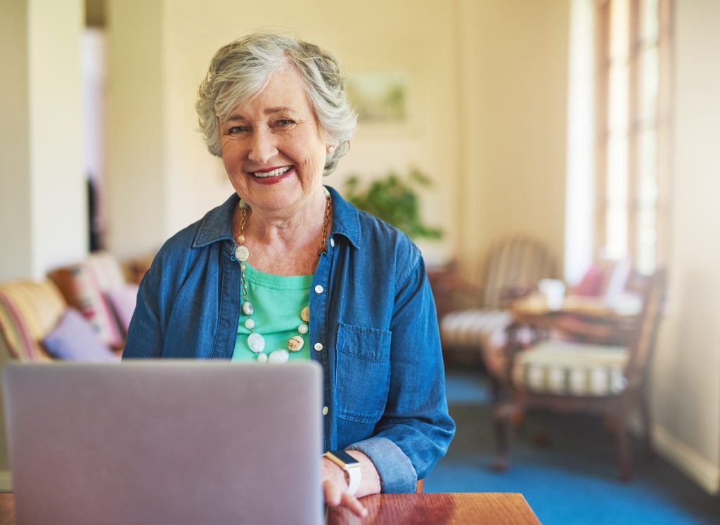 A old woman smiling in front of a laptop