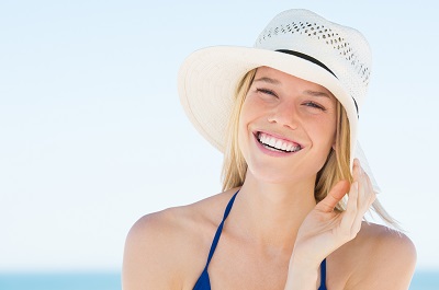 Portrait of smiling woman on beach wearing blue bikini and straw hat.