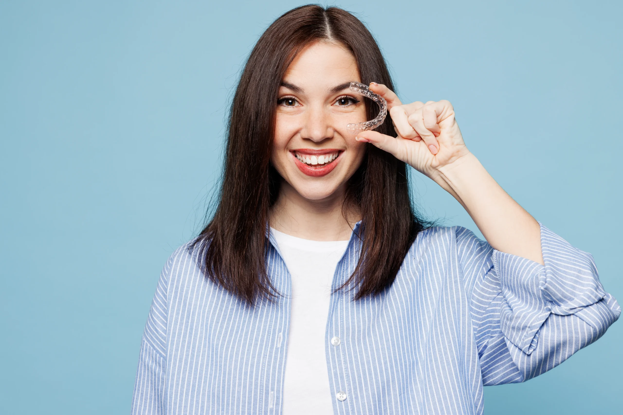 Woman smiling and holding Invisalign clear aligner